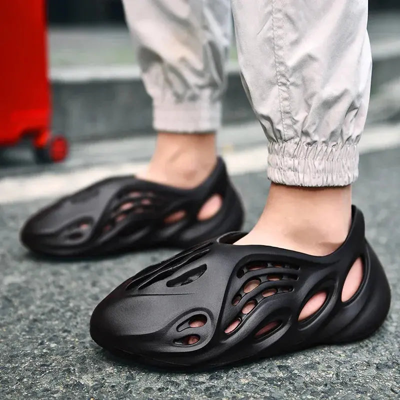 Black slip-on foam clogs with cutout design, worn outdoors with light joggers