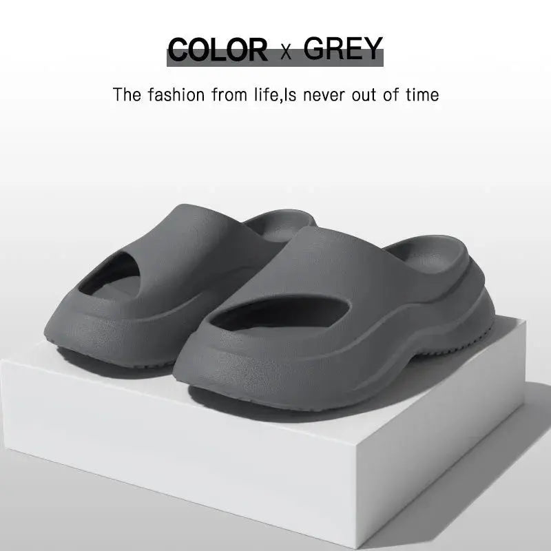 Grey slip-on foam sandals with open toes, minimalist design, displayed on a white box.