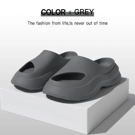 Grey slip-on foam sandals with open toes, minimalist design, displayed on a white box.