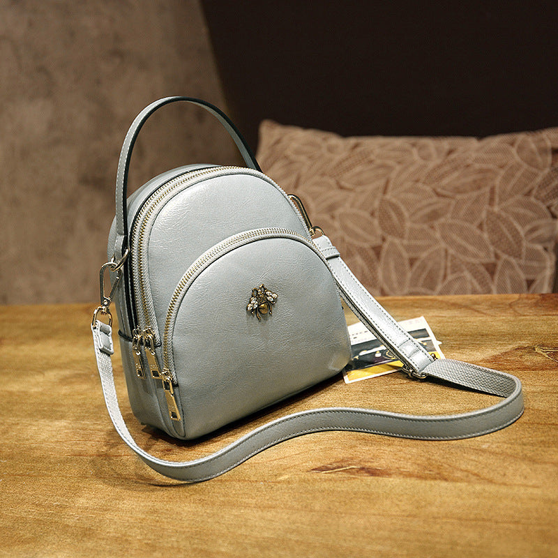 Undefyning Lynes oil wax leather convertible shoulder bag in light grey with a bee emblem and adjustable strap.